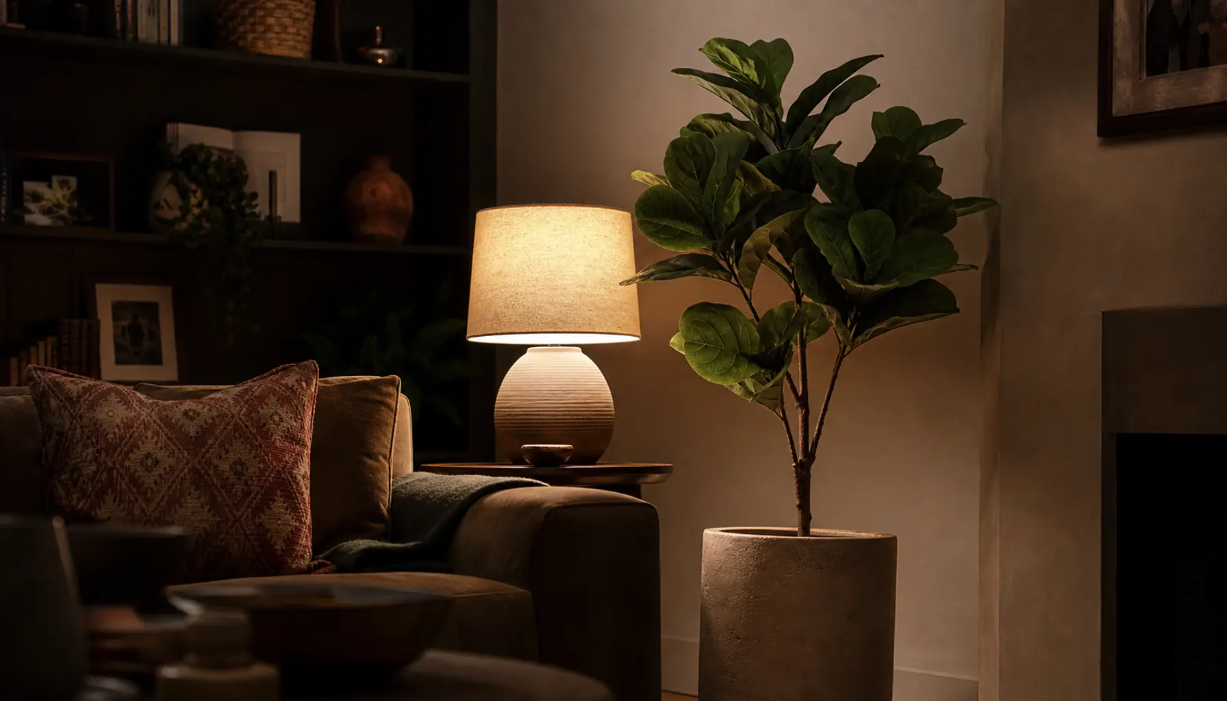 A dark living room corner warmed by a faux fiddle-leaf fig beside a lamp in a ceramic pot